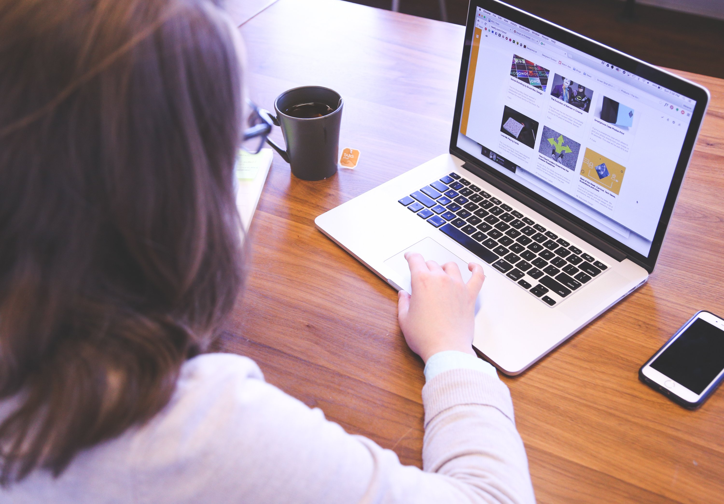 Canva - Woman Swiping Touchpad on Macbook Pro on Table Near Smartphone and Mug